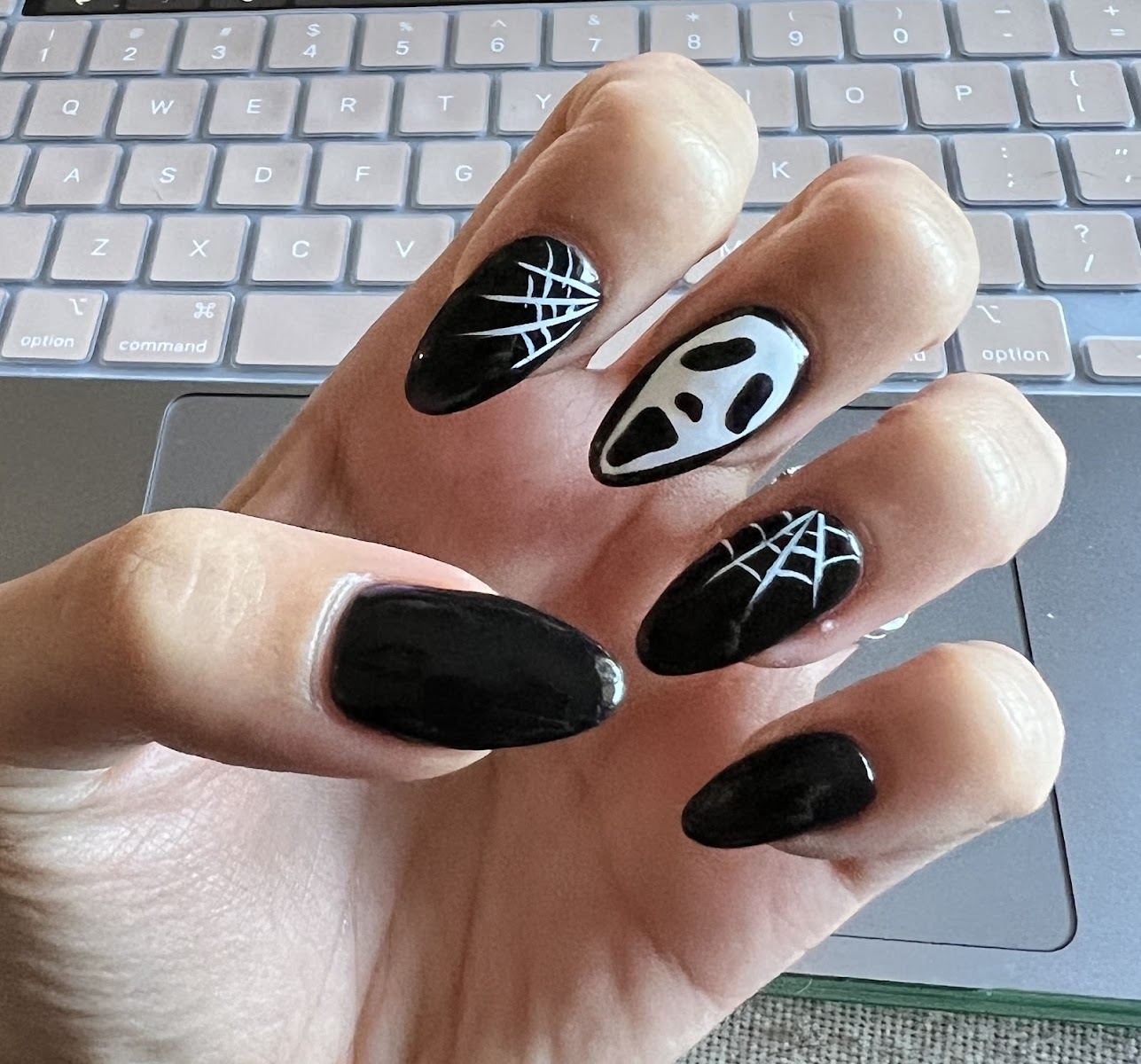 Glossy black almond nails with white spiderweb and ghost face art