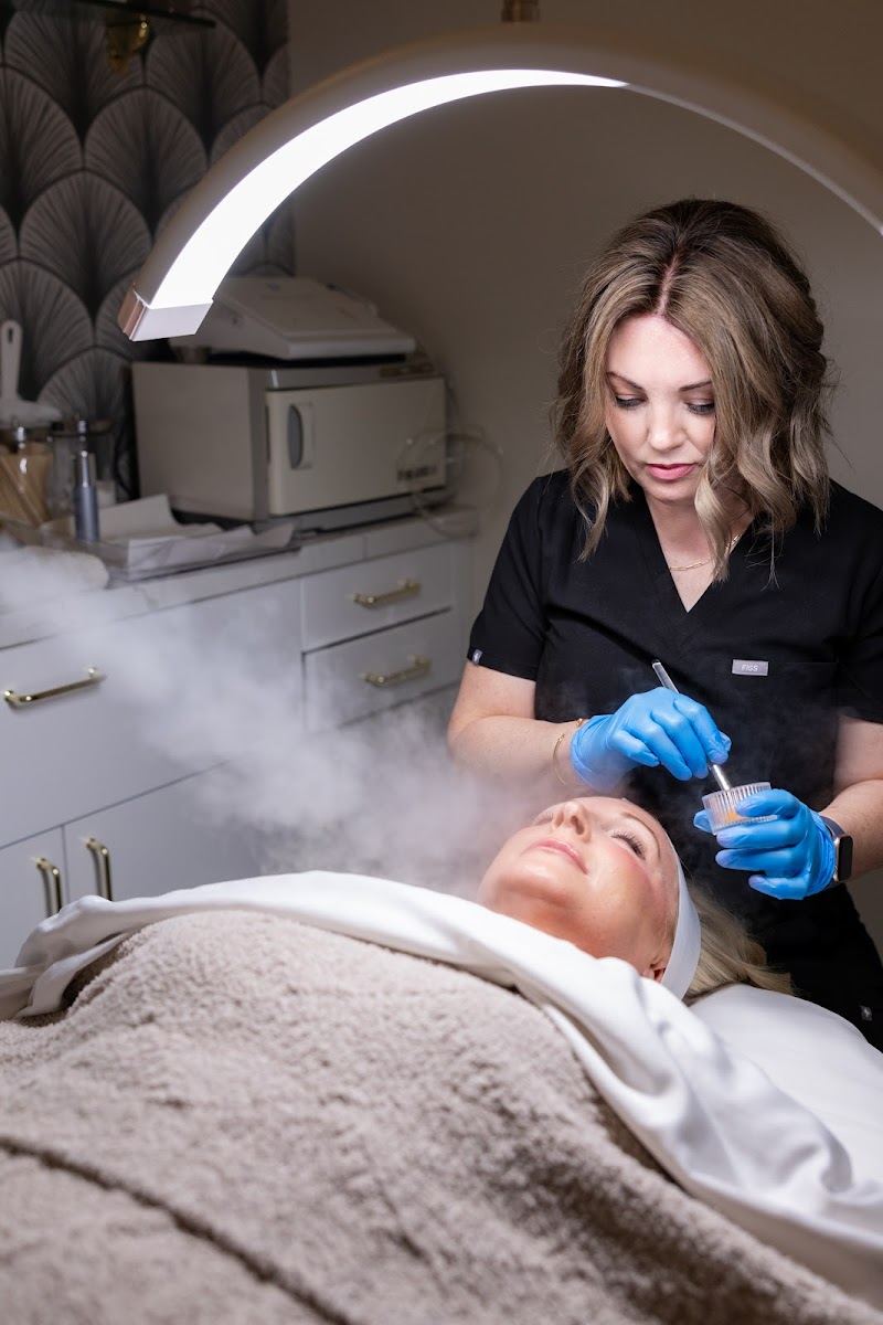 Aesthetician applying a treatment under a facial steamer in the treatment room