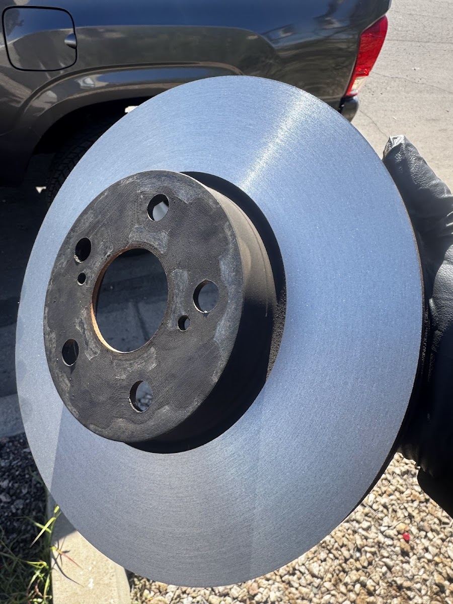 New brake rotor held up beside a vehicle