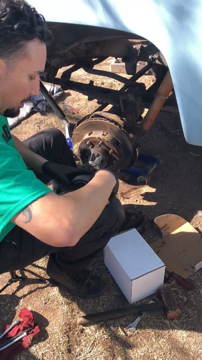 Mechanic in a green shirt working under a white truck at a wheel hub