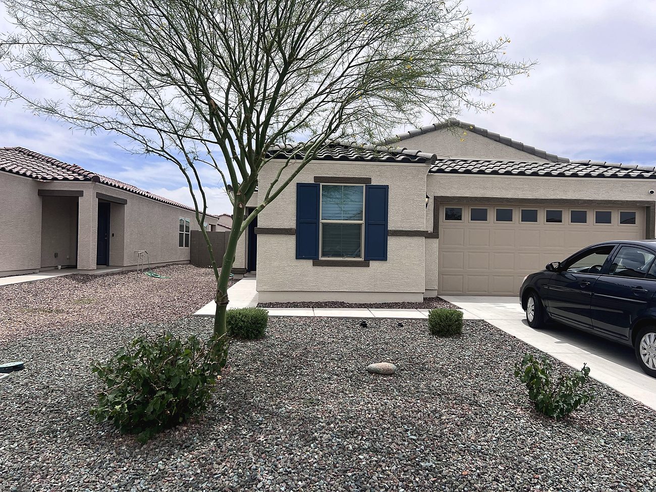 A front yard of fresh gravel with small shrubs and a desert tree in front of a tan house