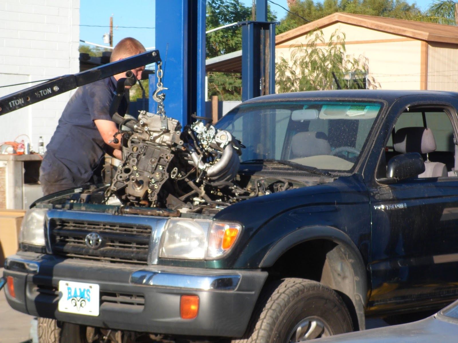 A B & H mechanic working on the engine of a green pickup truck outside the shop