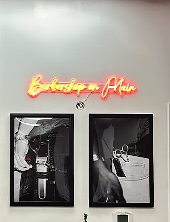 The orange neon script sign reading Barbershop on Main above two framed black and white photos of barber tools