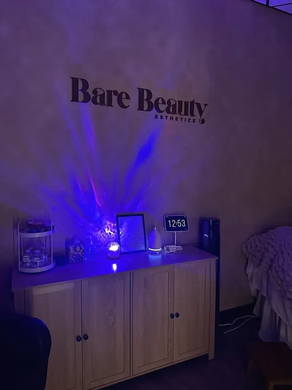 The Bare Beauty Esthetics wall sign lit in blue light above a wood cabinet