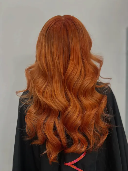 Bright copper hair in soft waves, seen from the back over a black cape