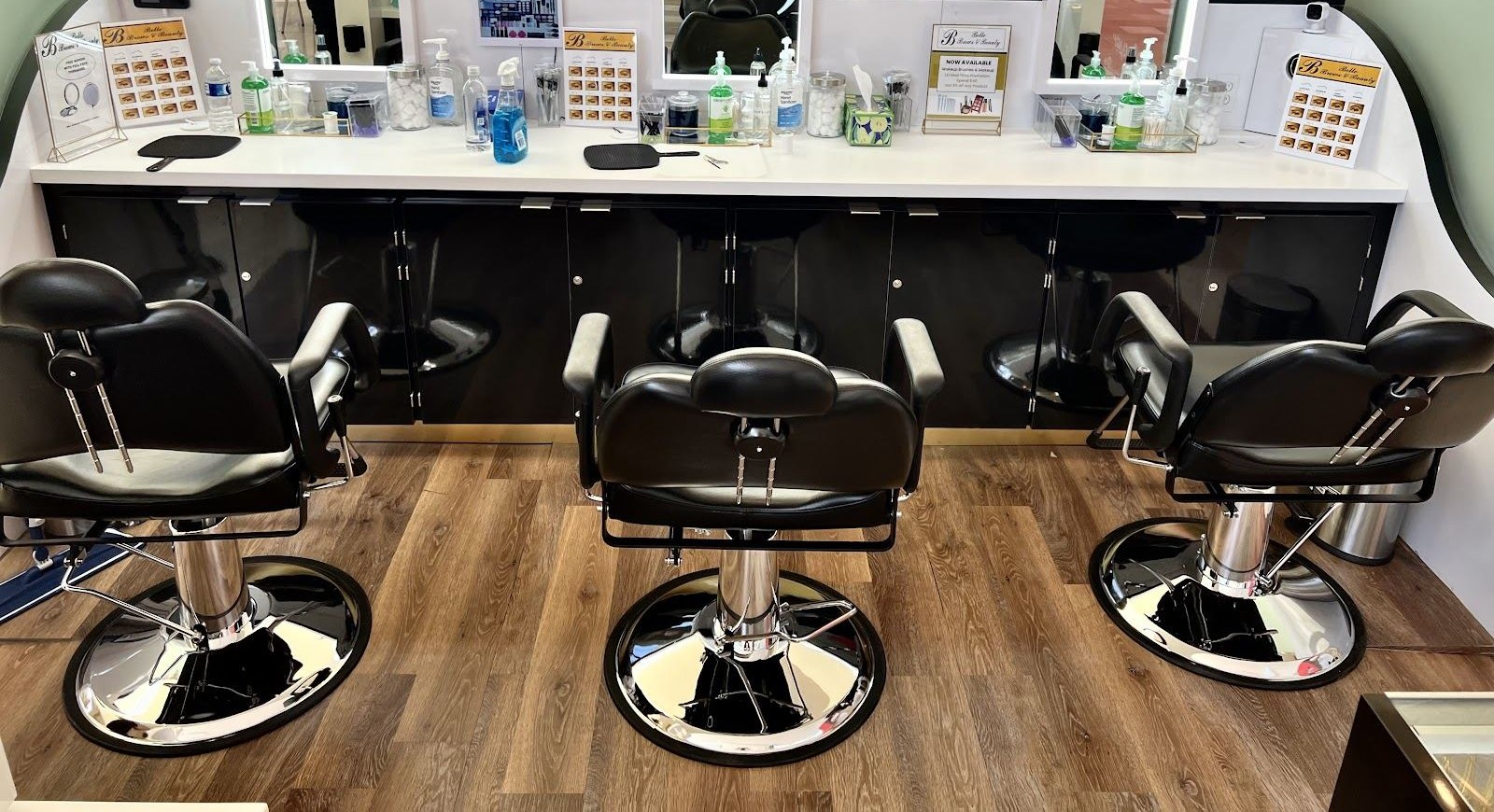 Three black salon chairs facing the mirrored station at Belle Brows and Beauty