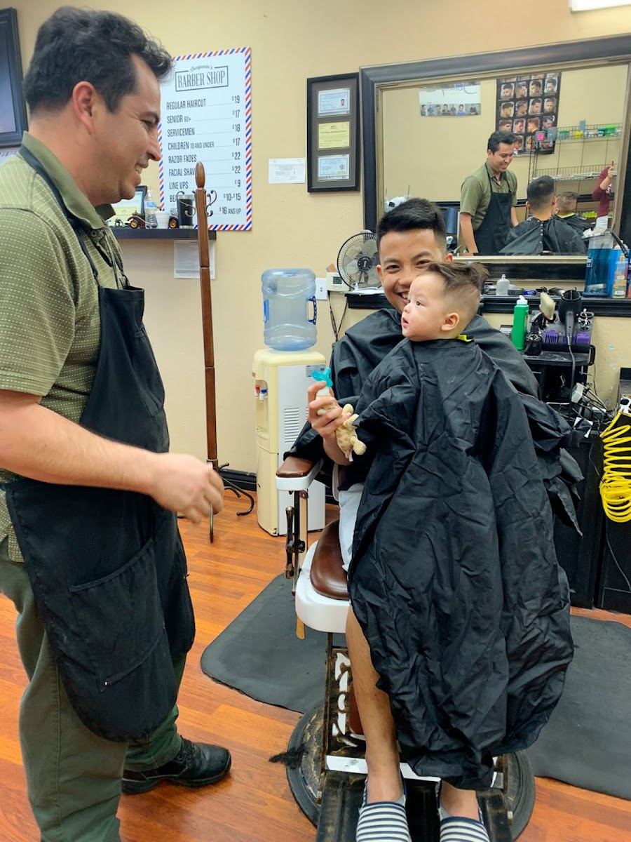 A barber at Benjamin's standing beside a young boy in a black cape in the barber chair