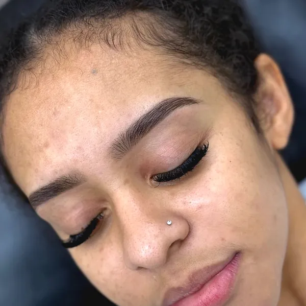 A woman with eyes closed and a small nose stud, clean tinted brows and long lashes