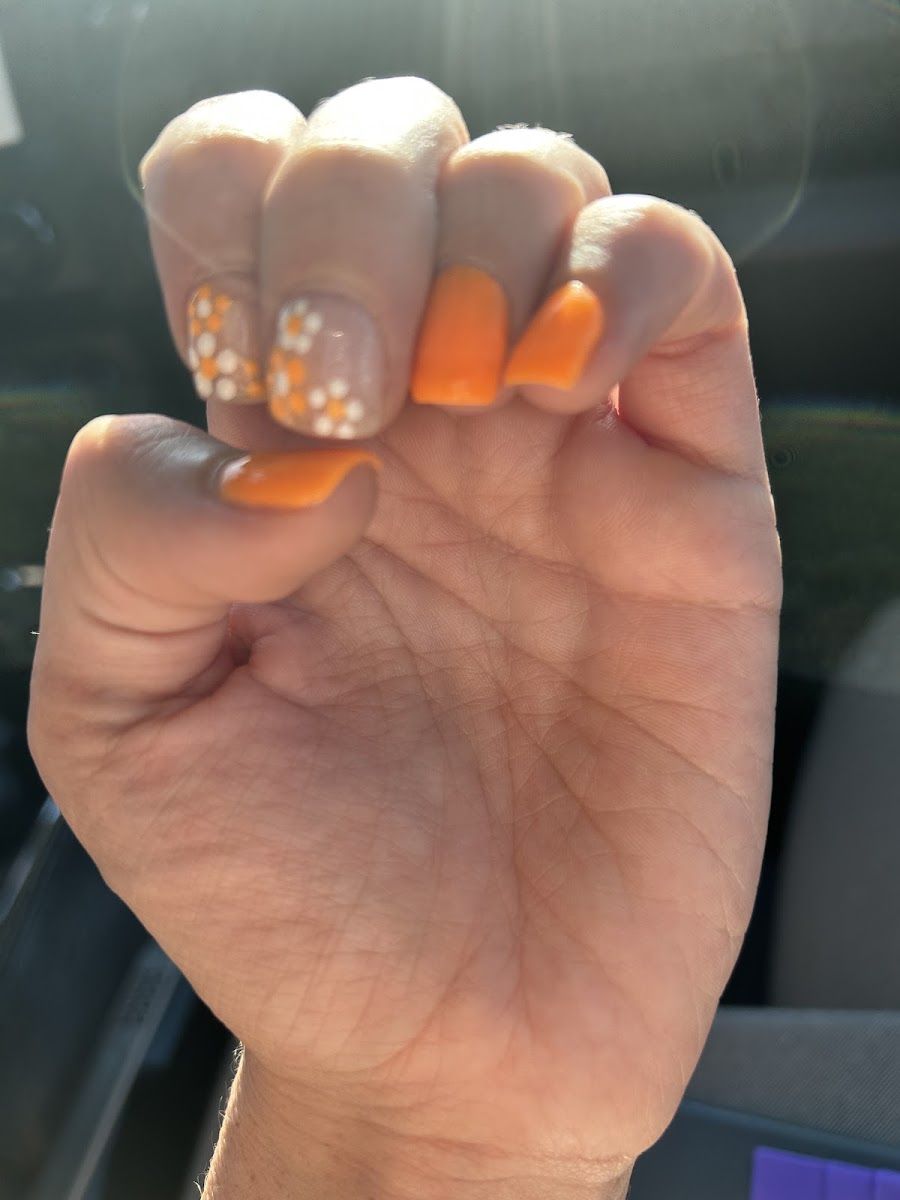 Short orange nails with white flower art on two fingers