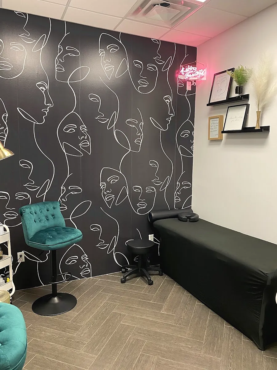 Brandi's suite: black wallpaper with white line drawn faces, a pink neon sign, a teal velvet chair and a black treatment bed
