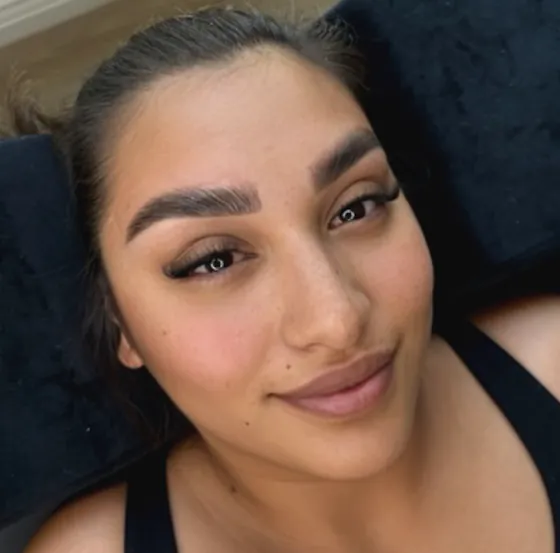 A woman lying back on a black treatment bed with full, brushed-up brows and lifted lashes