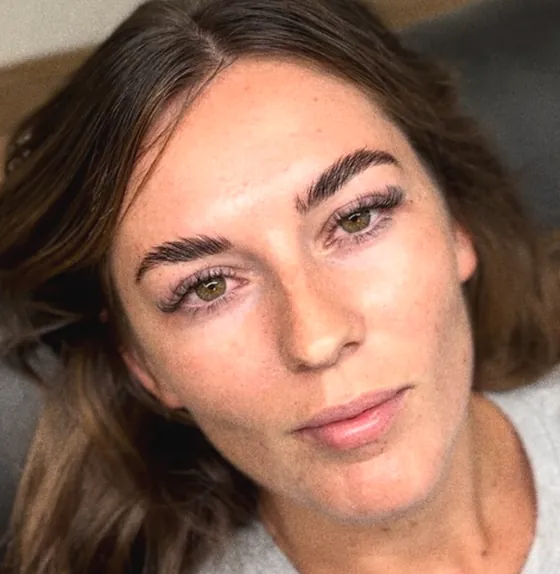 Close portrait of a woman with freckles, defined brushed-up brows and lifted lashes