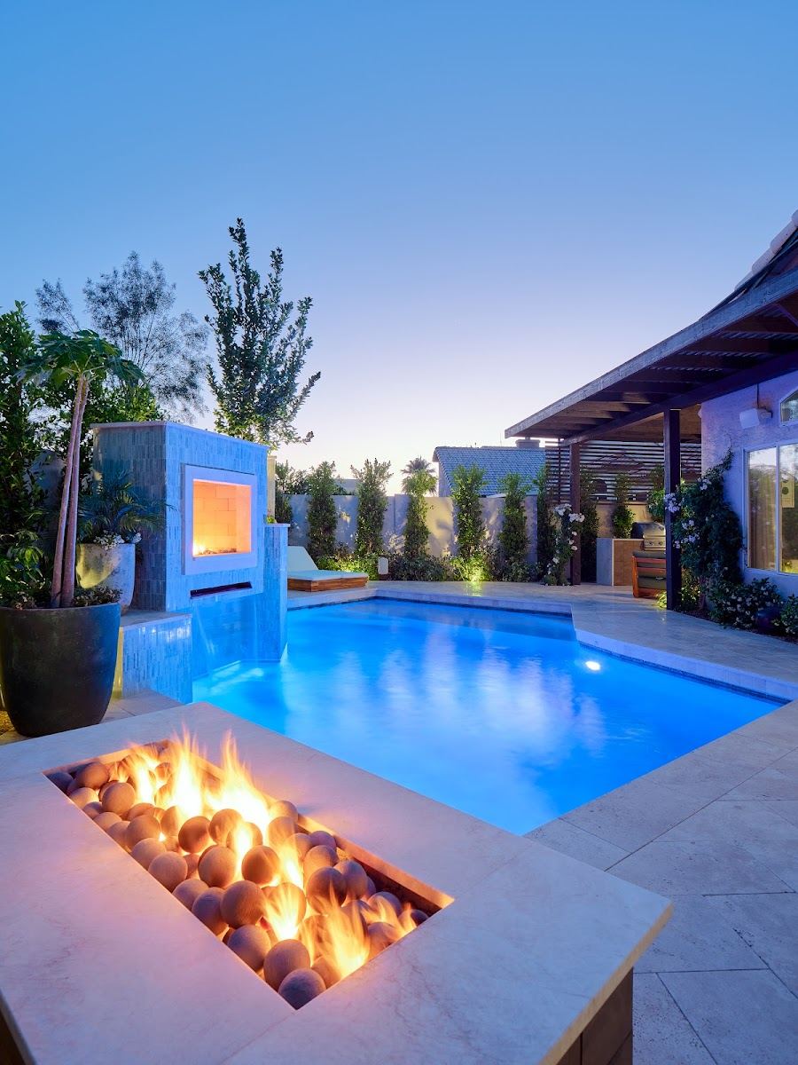 Pool with a lit water feature and a linear fire pit at dusk