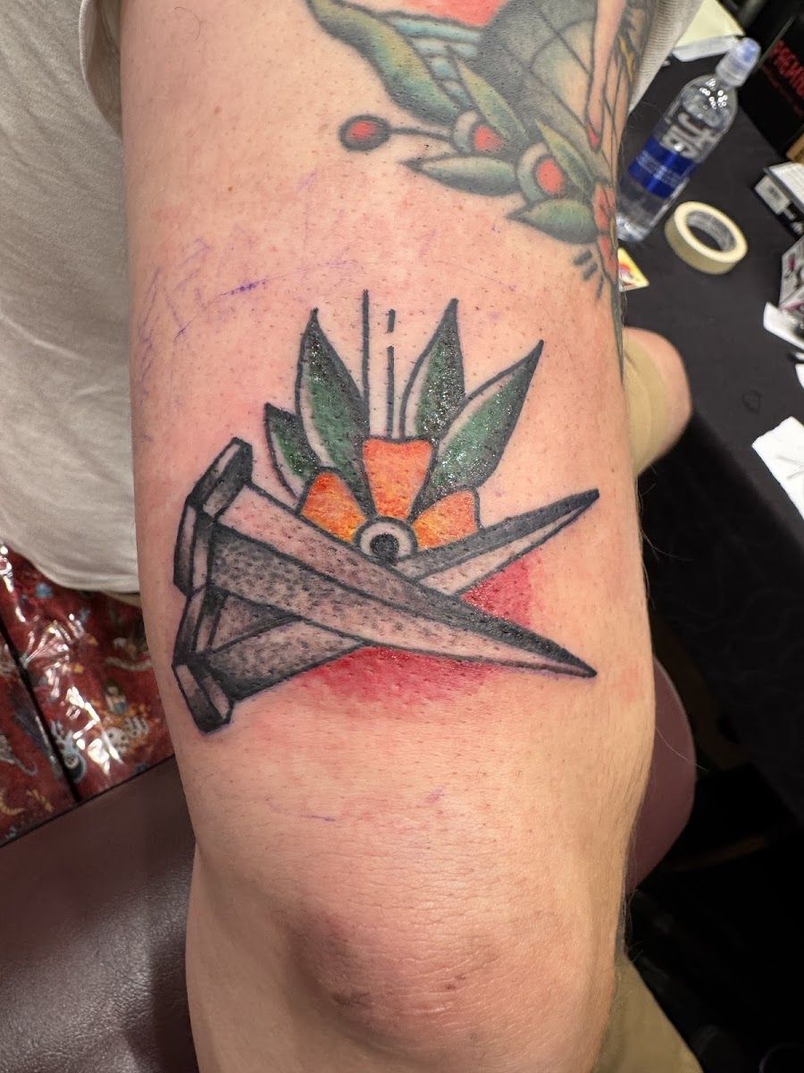 Bold color tattoo of a paper plane with leaves