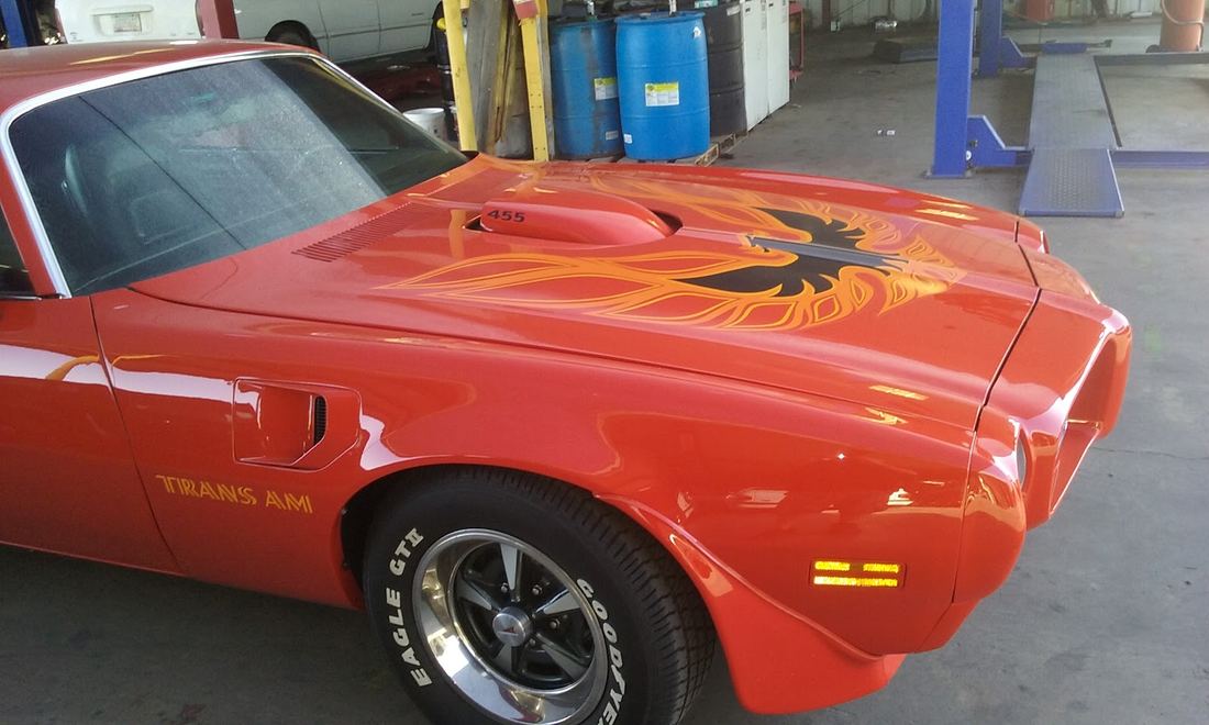 Orange classic Pontiac with a firebird hood graphic in the shop