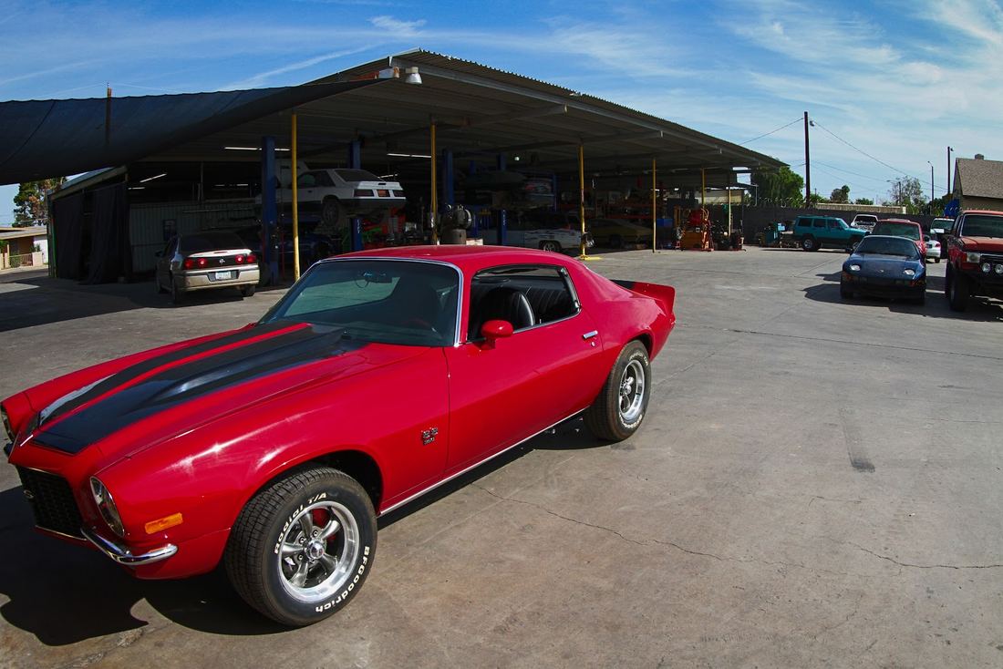 Red classic Camaro with black stripes parked by the shop