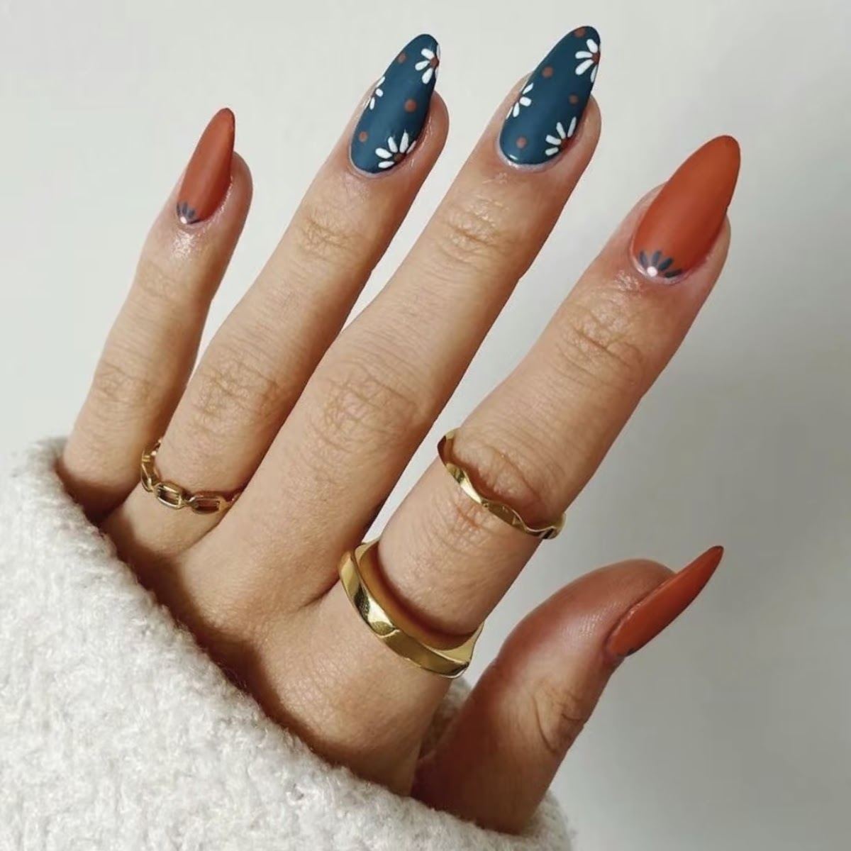 Almond nails in burnt orange with two navy accent nails painted with white daisies