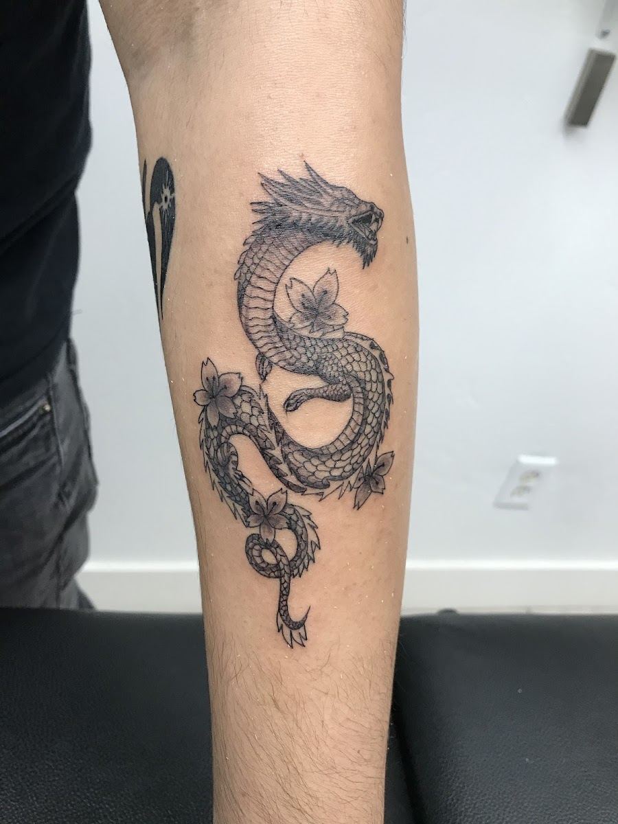 Black and grey dragon tattoo winding down a forearm with peony accents
