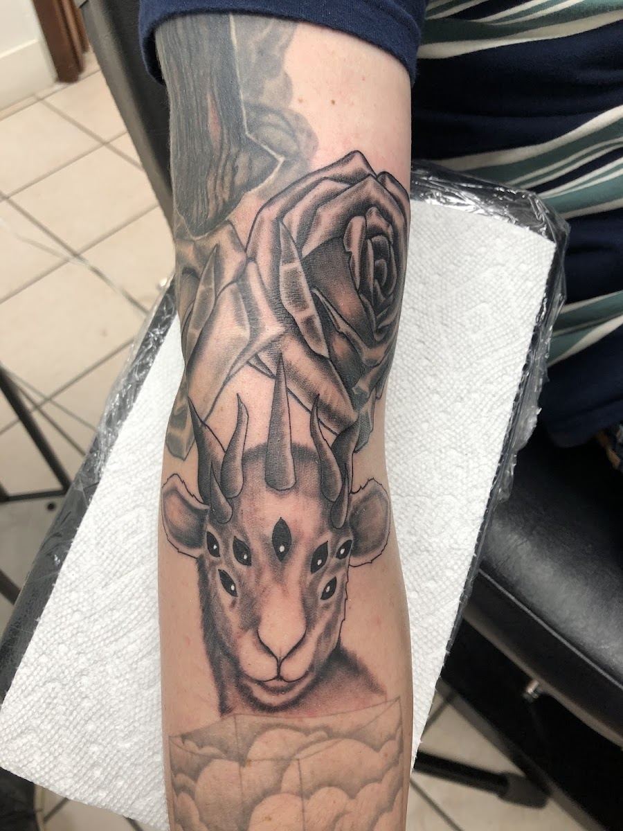 Black and grey forearm tattoo of a horned animal beneath large roses