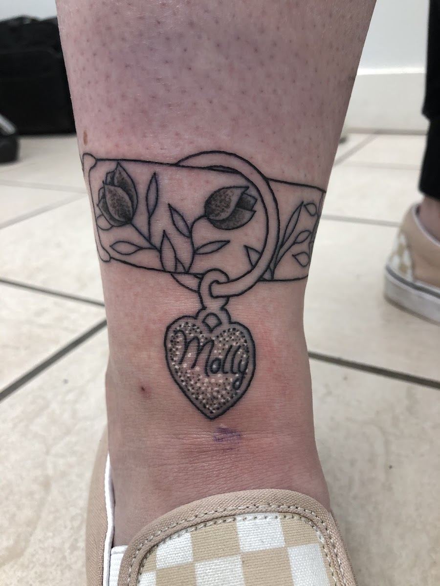 Ankle band tattoo with leaves and a heart charm reading Molly