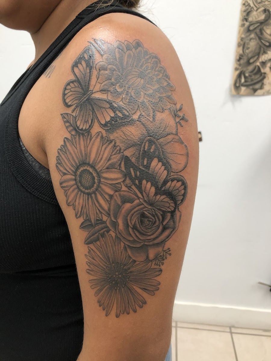 Black and grey floral shoulder tattoo with daisies, roses and a butterfly