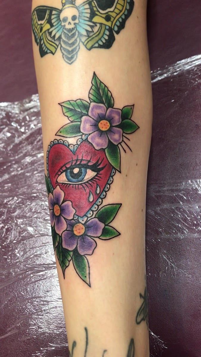 Sacred heart with an eye and purple flowers on a forearm