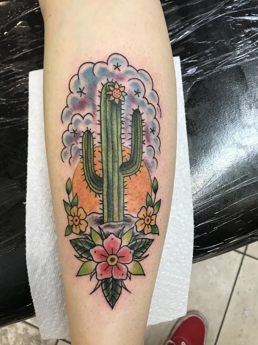 Traditional saguaro cactus tattoo with flowers and a desert sun on a forearm