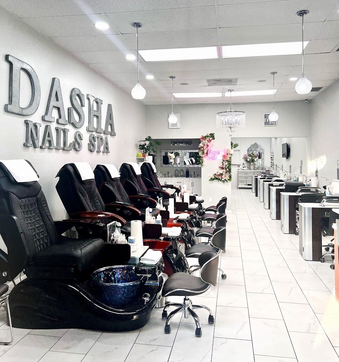 Inside Dasha Nails and Spa: a row of black pedicure chairs under the silver DASHA NAILS SPA sign
