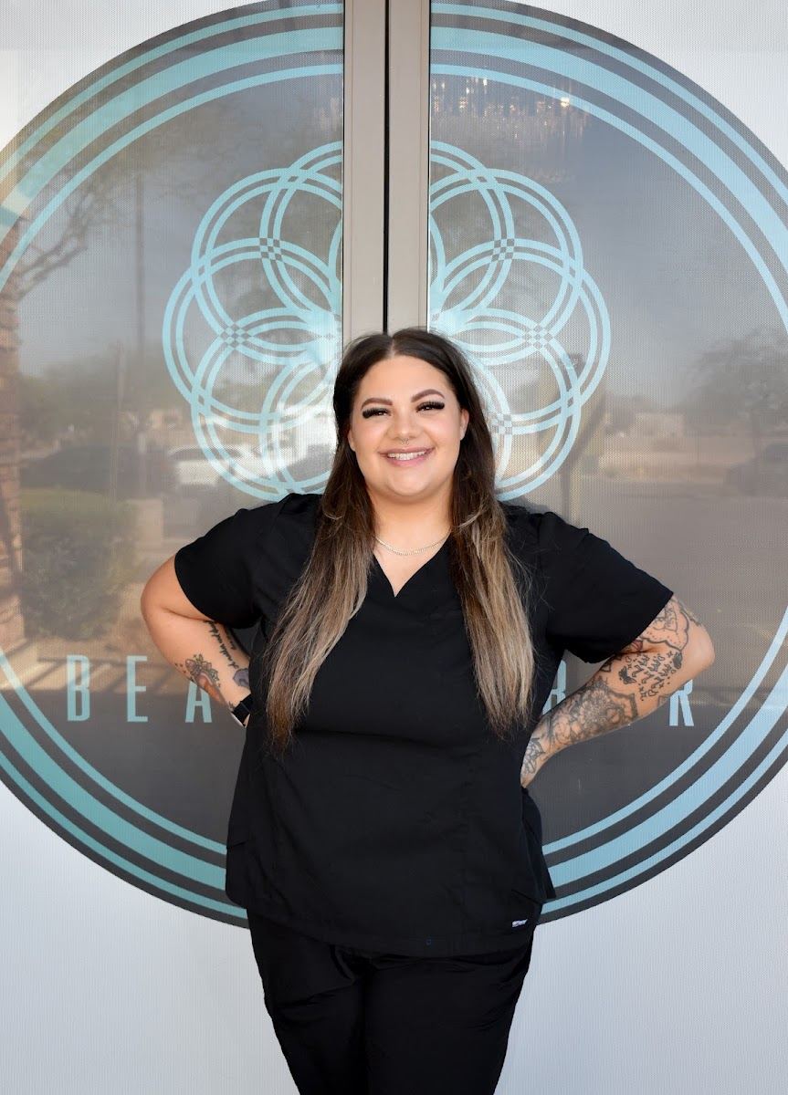 A team member standing in front of the teal mandala wall logo