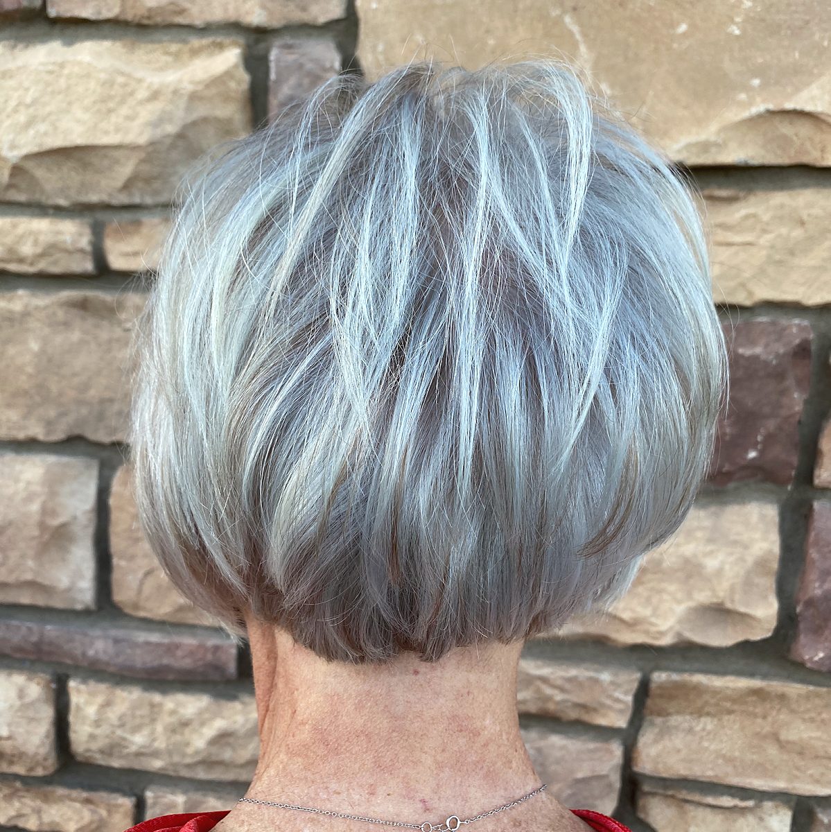Back of a short, stacked bob in bright silver and gray against a stone wall