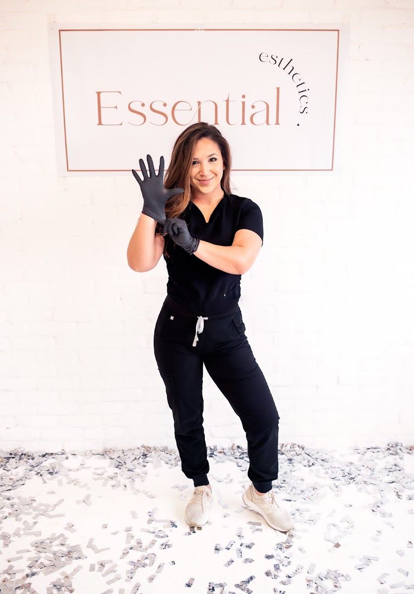 Carey, esthetician, standing in front of the Essential Esthetics sign
