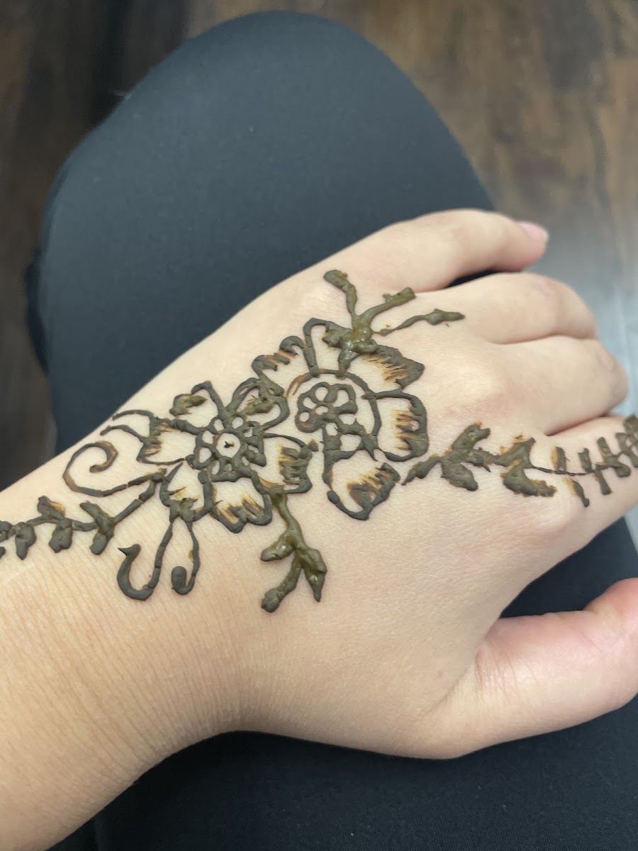 Hand-drawn floral henna design on the back of a client's hand