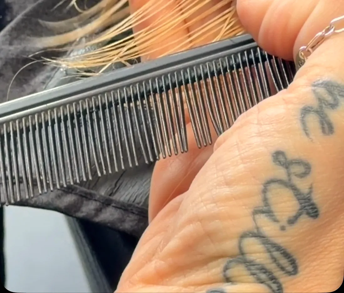 Close up of shears cutting a straight line through blonde ends held over a fine comb