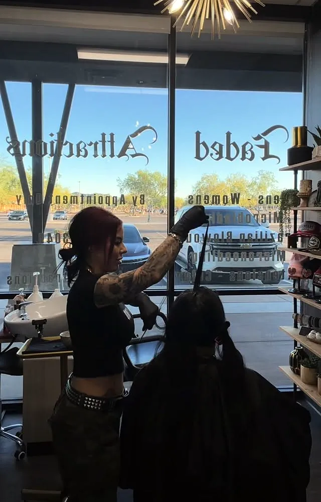 Becca at work by the front windows, with the Faded Attractions blackletter decal on the glass and a gold starburst light overhead