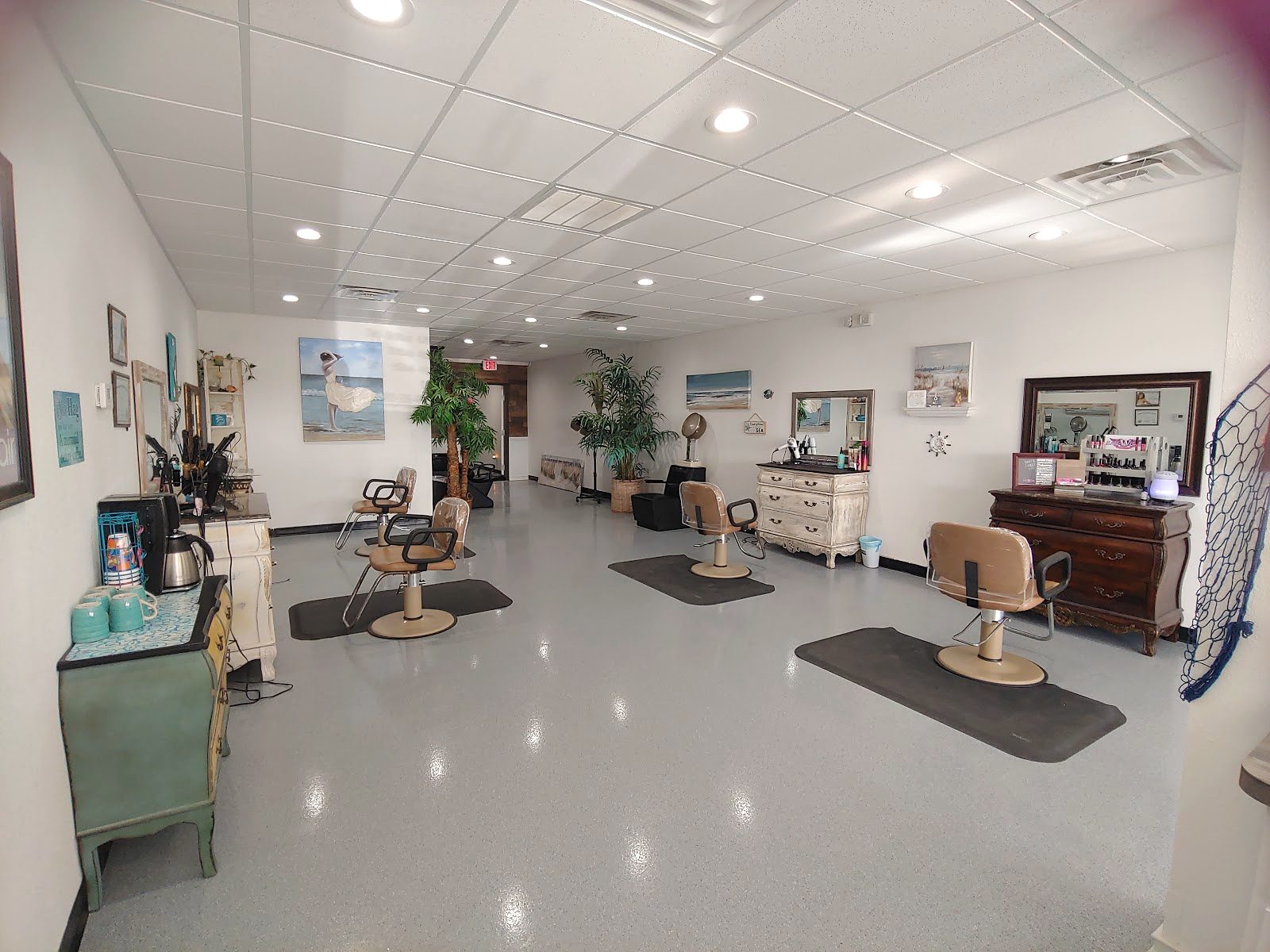 A bright salon floor with styling chairs, mats, plants and framed art on white walls