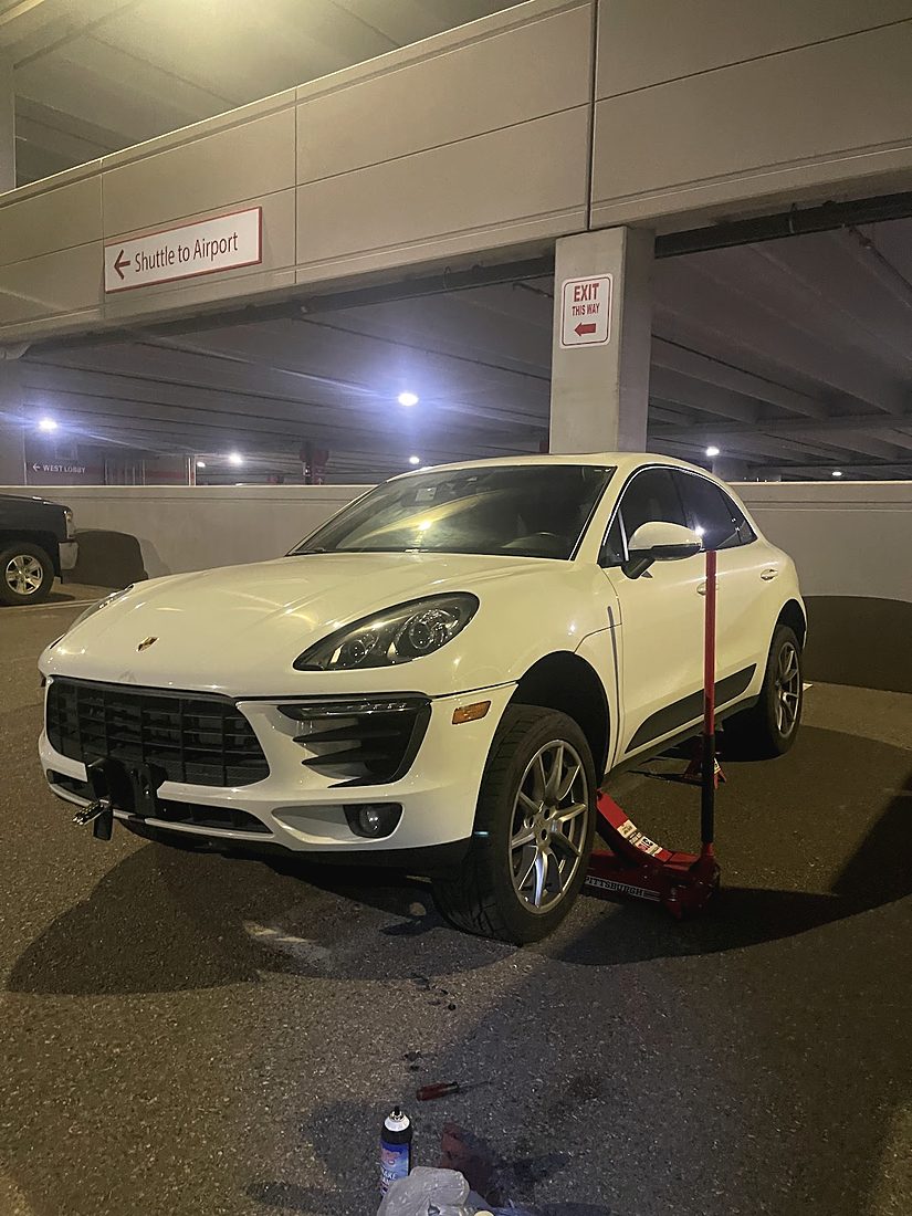 A white Porsche SUV on a red floor jack in a parking garage