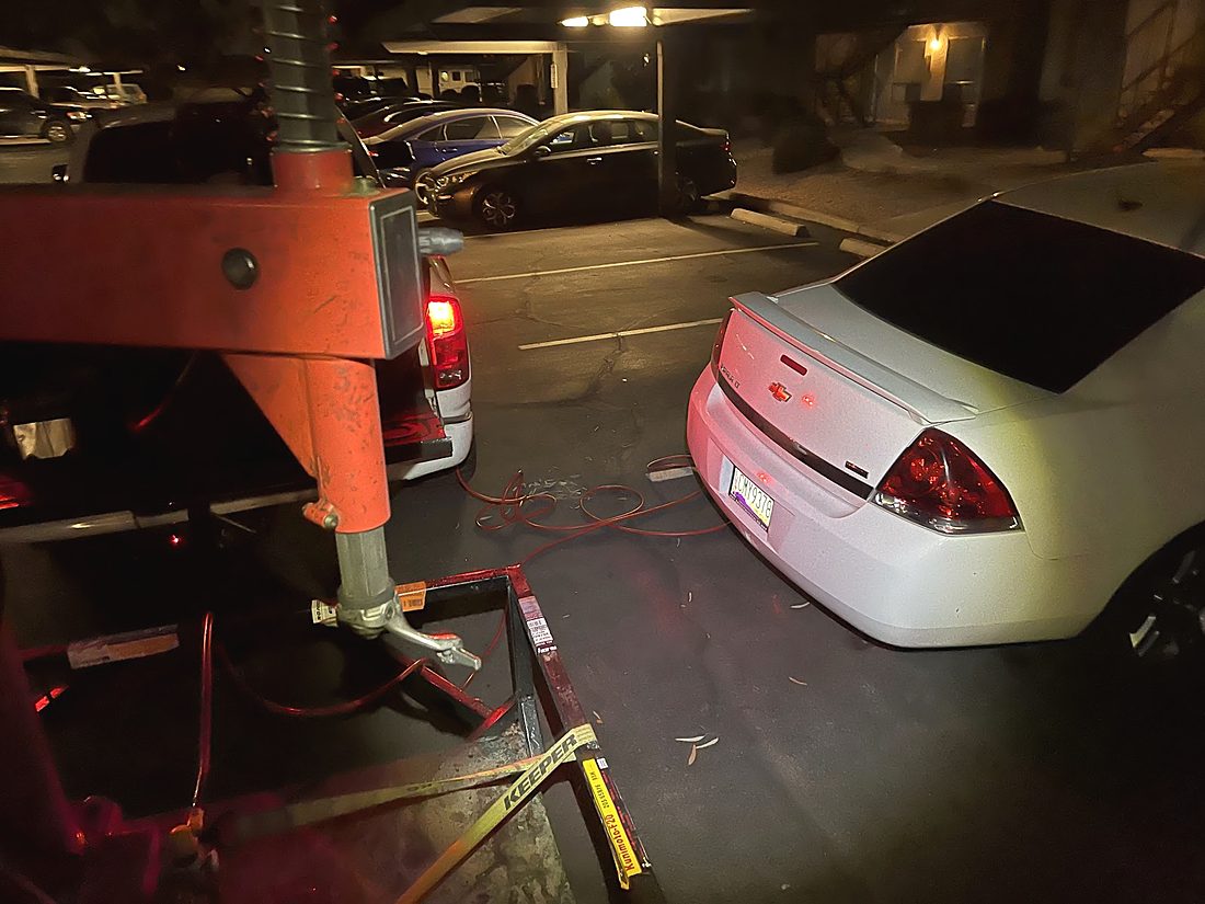 Work at night: the red tire machine on a trailer beside a white sedan in a lit parking lot