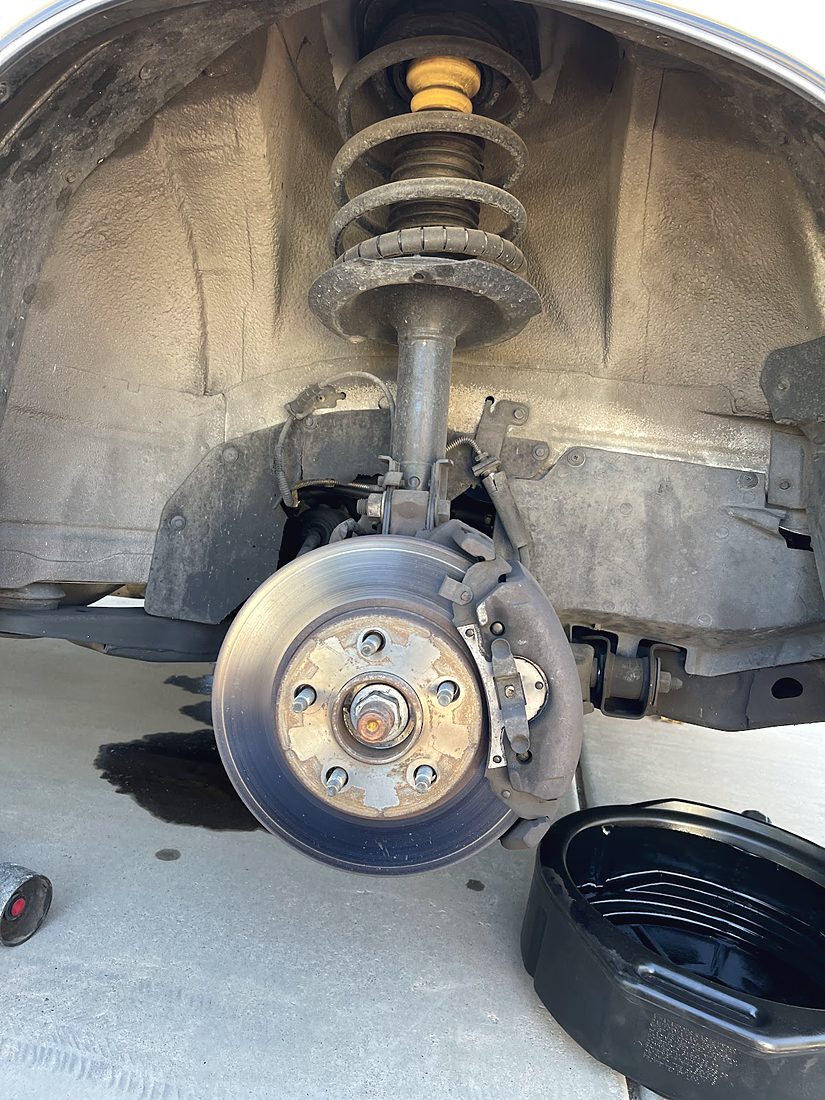 A coil spring strut and brake rotor installed in an open wheel well, wheel removed