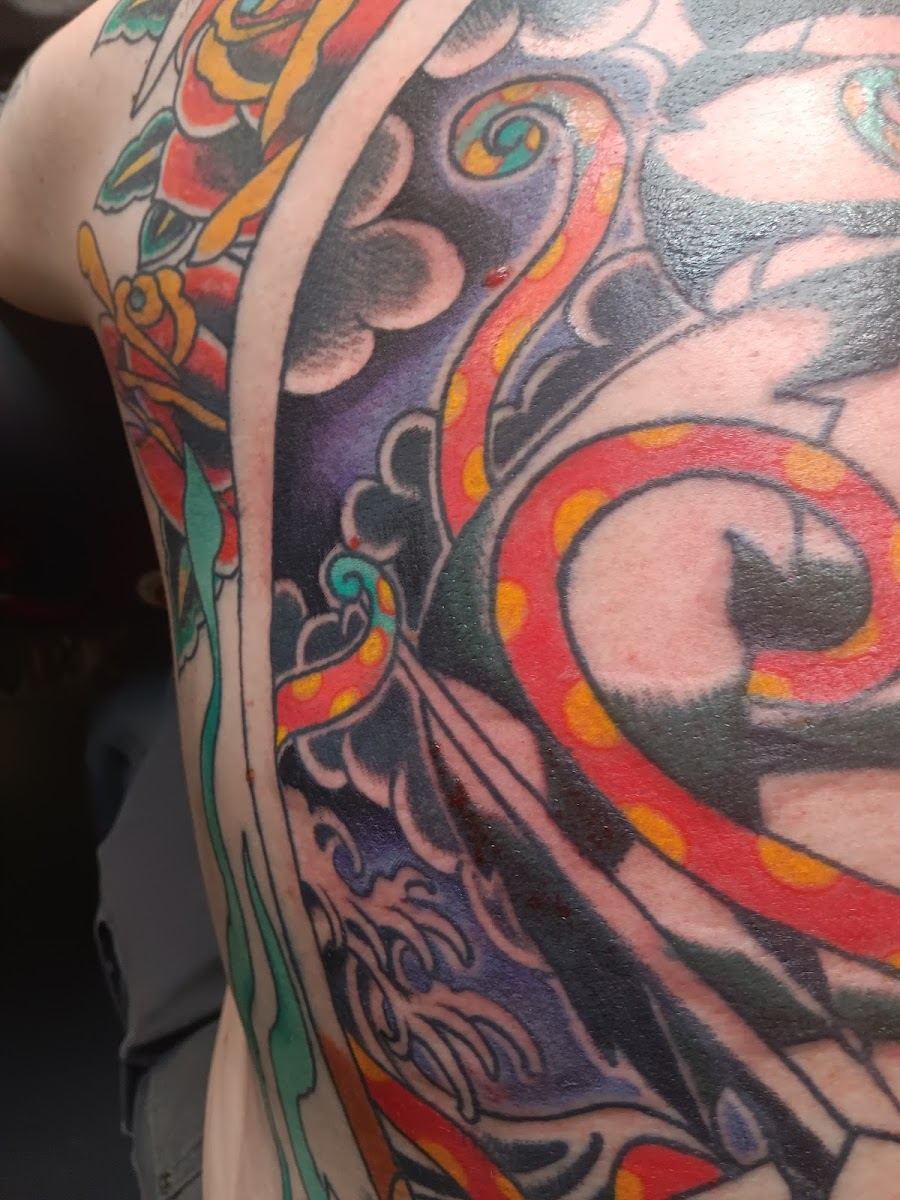 Close up of a bold color tattoo with red swirl, roses and purple shading