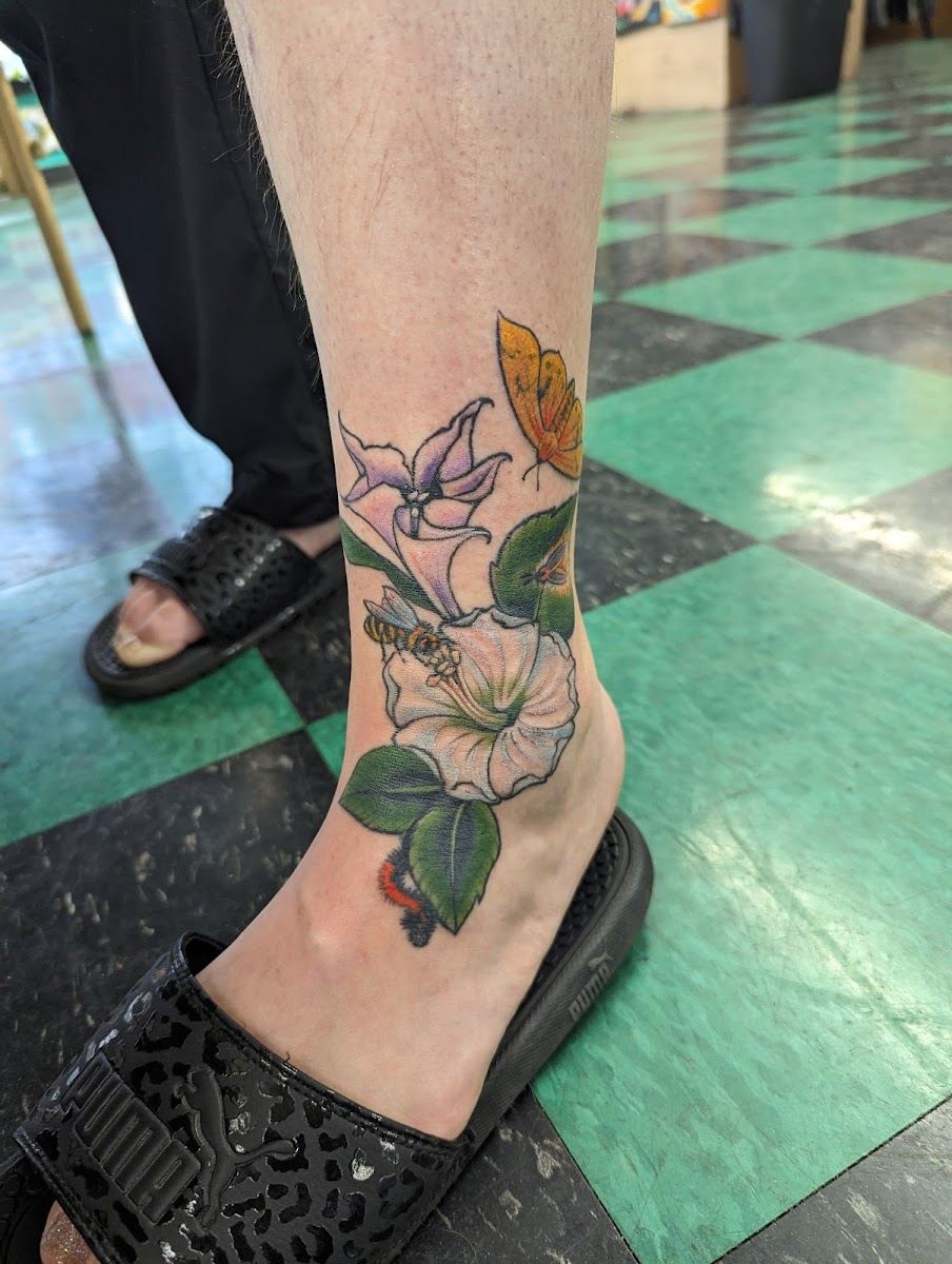 Fresh color floral tattoo with leaves on an ankle, on the shop's checkered floor