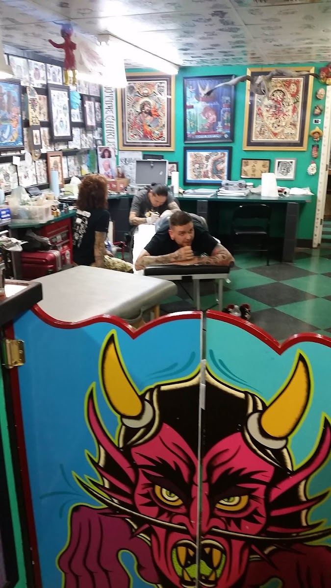 Inside Immaculate Tattoo: teal walls hung floor to ceiling with flash, a painted devil panel in front