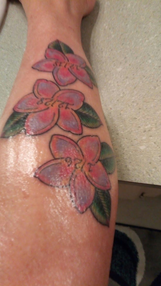 Pink flowers with green leaves tattooed on a forearm