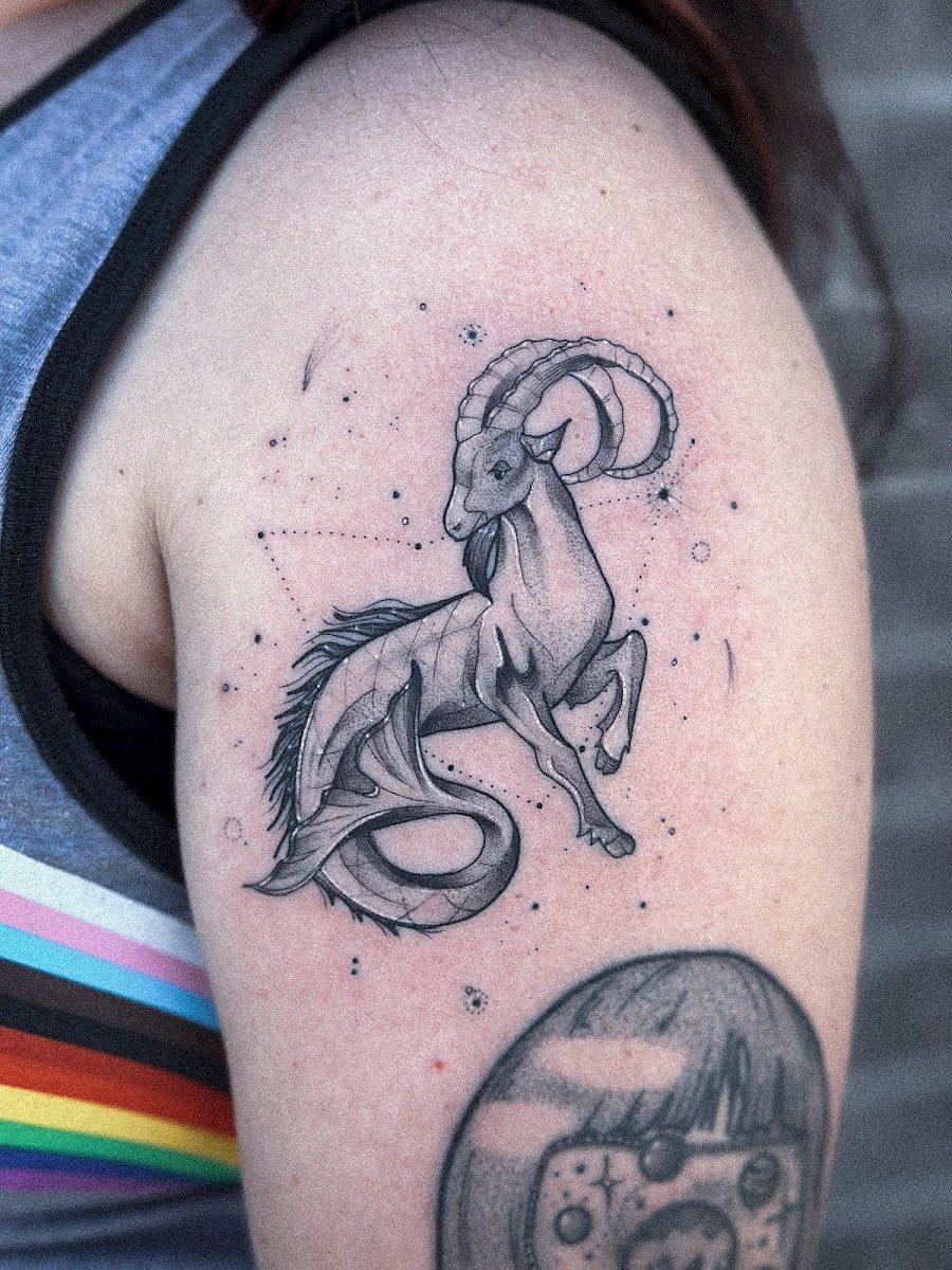 Sea goat with a curled fish tail among dots and stars, on an upper arm