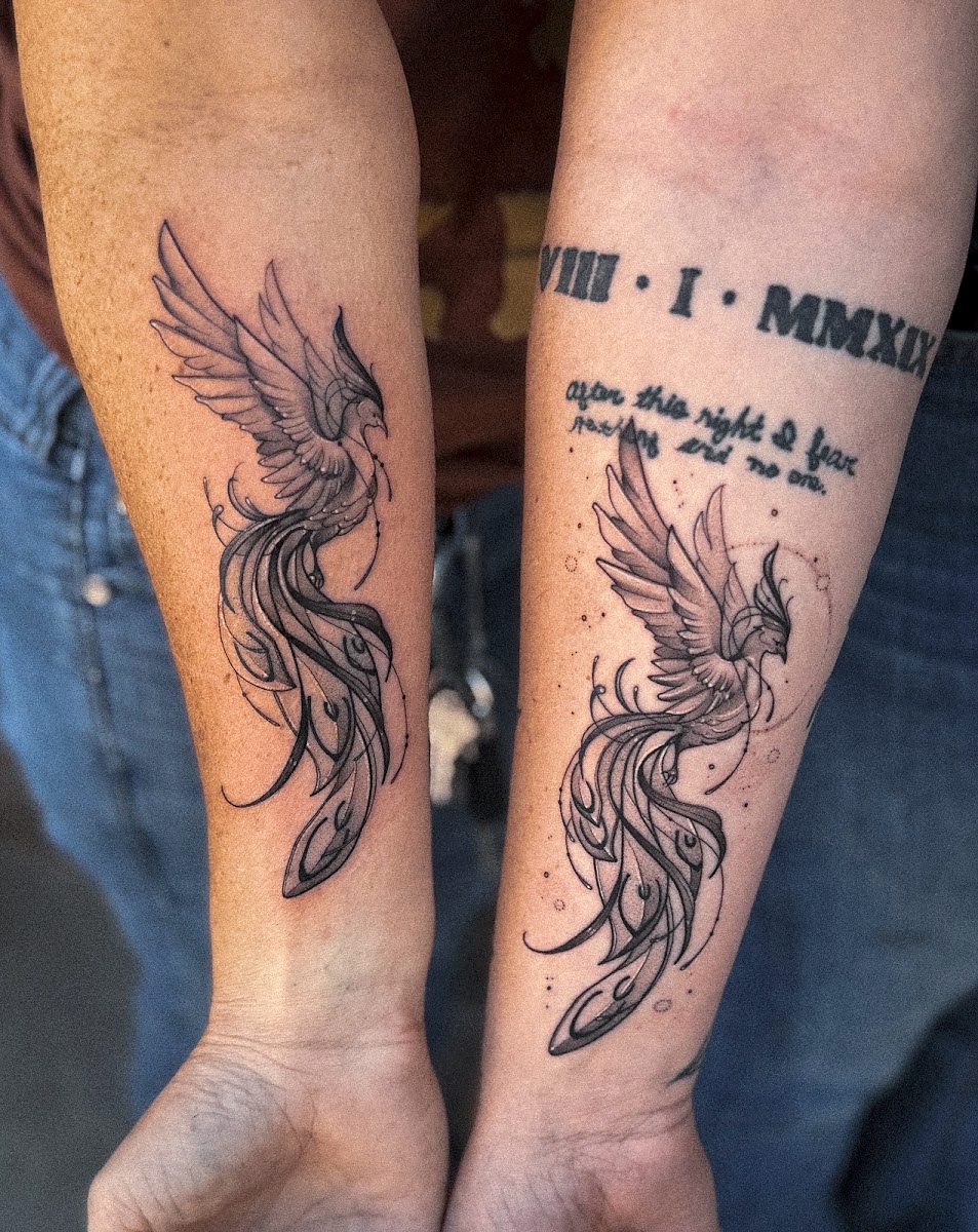 Two matching phoenix tattoos on two forearms, one with Roman numerals and script
