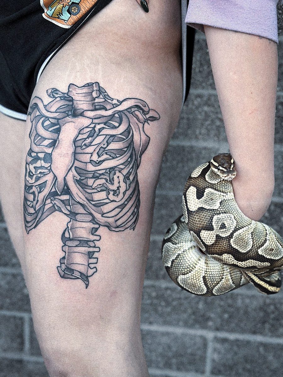 Anatomical ribcage and heart on a thigh, next to a pet snake