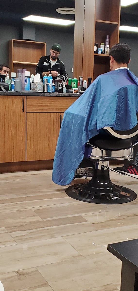 Client in a cape at a station with the barber working behind
