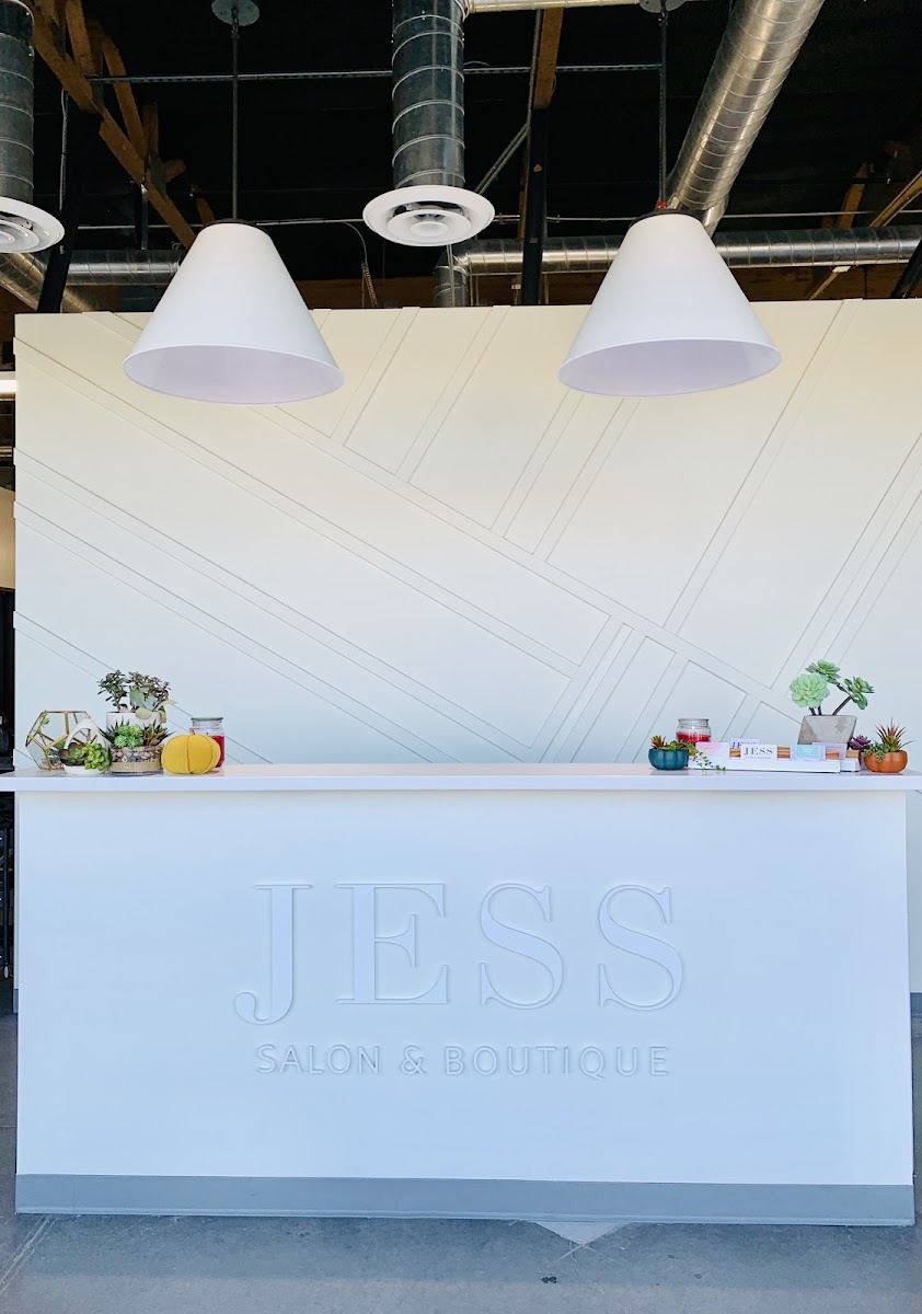 White reception desk with the JESS Salon & Boutique logo under two white pendant lamps