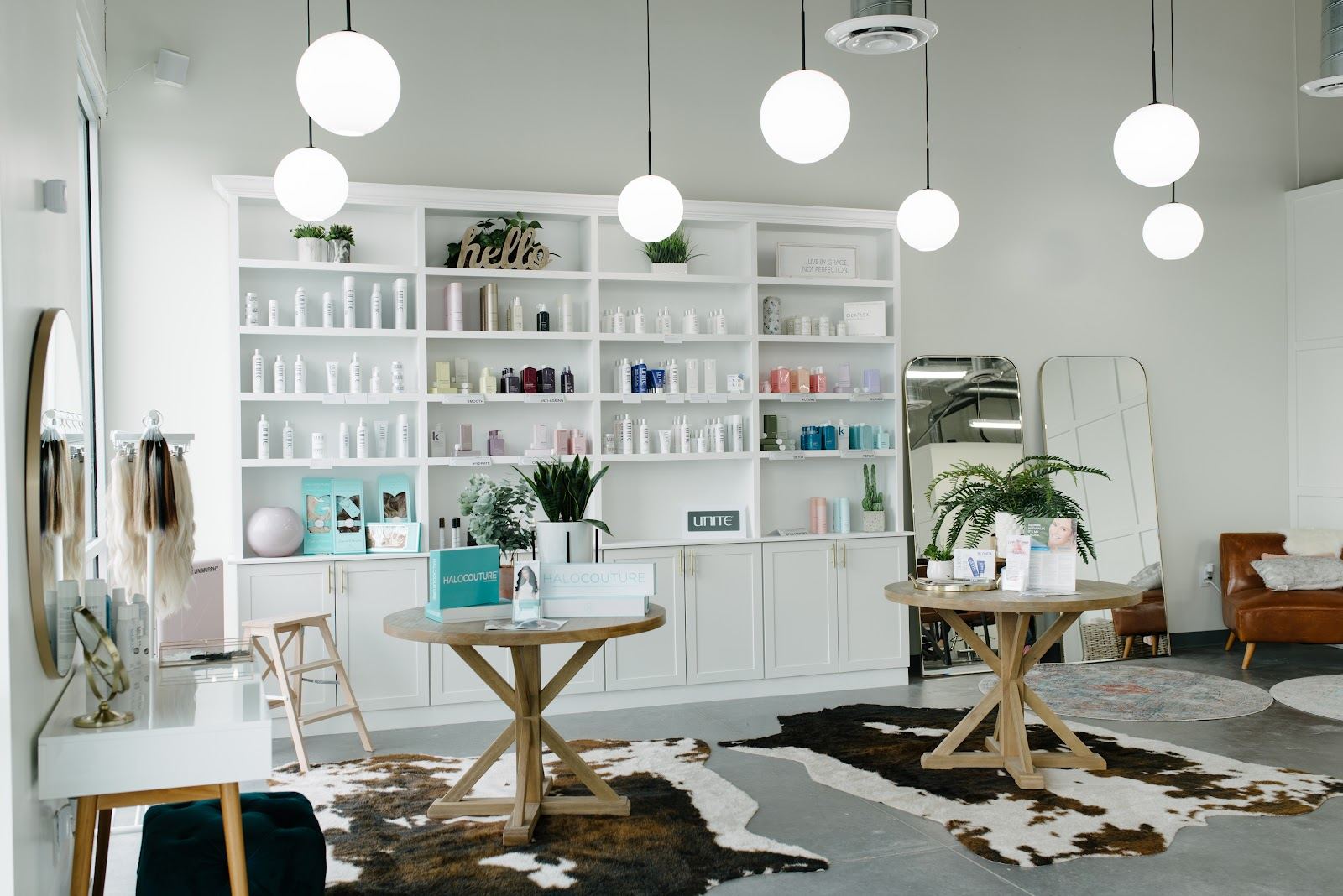 Jess Salon front room with white retail shelves, round wood tables, a cowhide rug and globe pendant lights