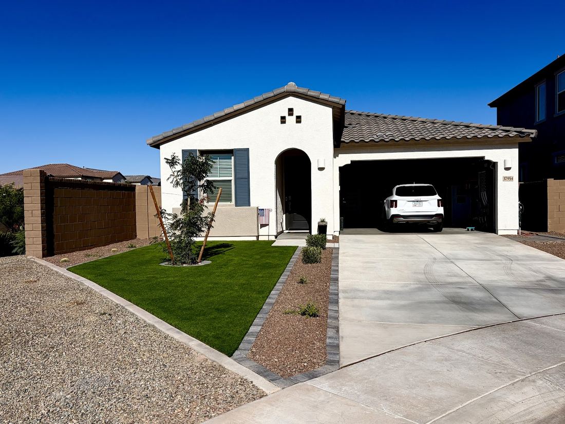 Front yard with turf, a young tree, rock beds and a paver edge beside the driveway