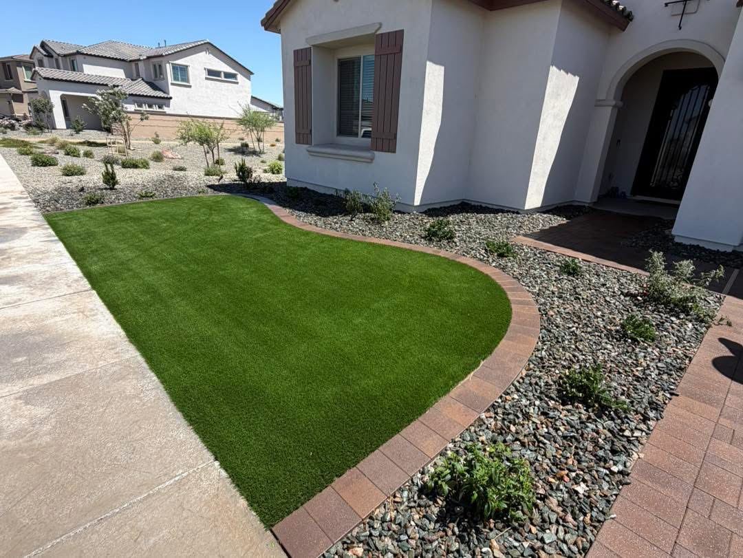 Curved turf lawn edged with red pavers next to a rock bed with desert plants
